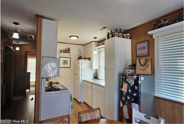 kitchen with washer / dryer, wood walls, hanging light fixtures, white refrigerator, and white cabinets