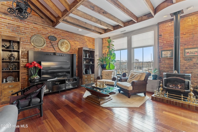 living room featuring wood-type flooring, beamed ceiling, brick wall, and a wood stove