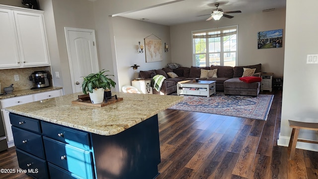 kitchen with dark wood-type flooring, light stone countertops, white cabinets, and a kitchen island