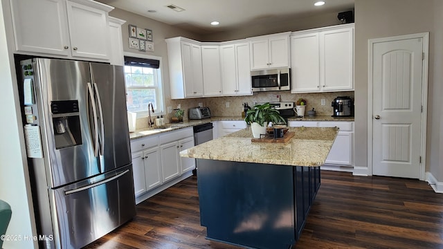 kitchen with a kitchen island, appliances with stainless steel finishes, white cabinetry, sink, and light stone countertops