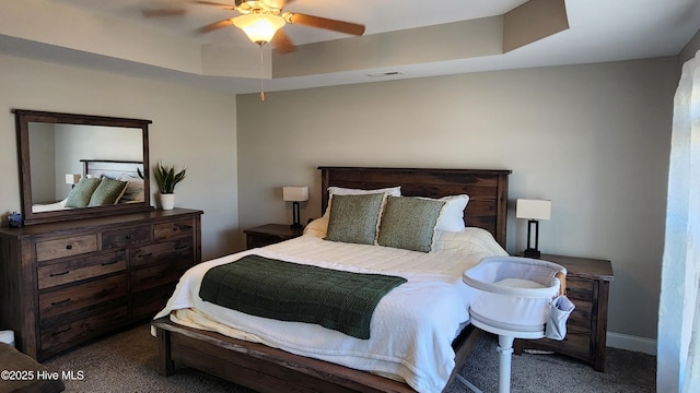 bedroom featuring a raised ceiling, ceiling fan, and dark colored carpet