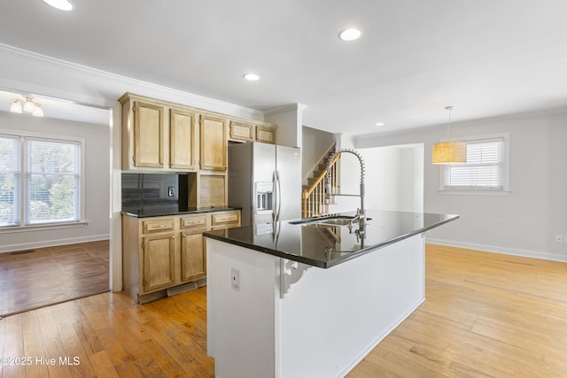 kitchen with hanging light fixtures, stainless steel fridge, light hardwood / wood-style floors, and a center island with sink