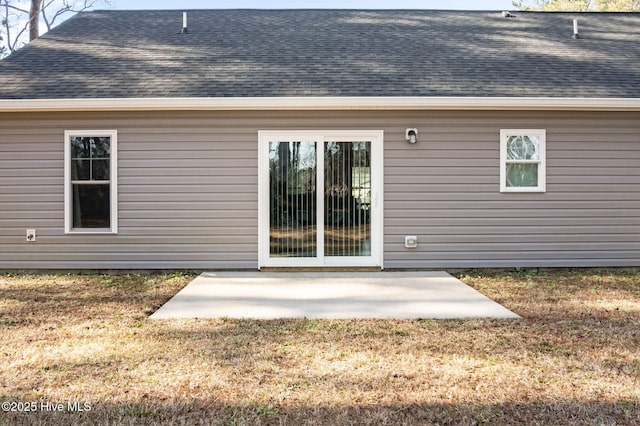 entrance to property with a shingled roof, a patio, and a yard
