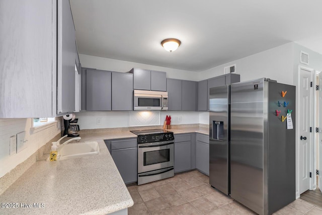 kitchen featuring stainless steel appliances, tasteful backsplash, gray cabinets, and sink