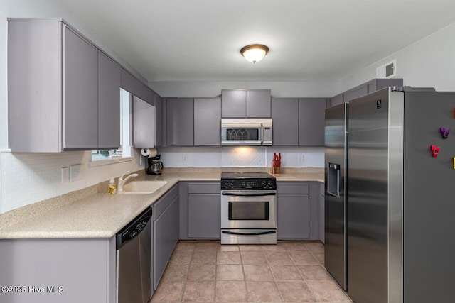 kitchen with gray cabinetry, sink, backsplash, and stainless steel appliances