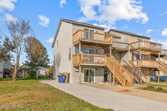 rear view of house featuring a wooden deck, a balcony, and a lawn