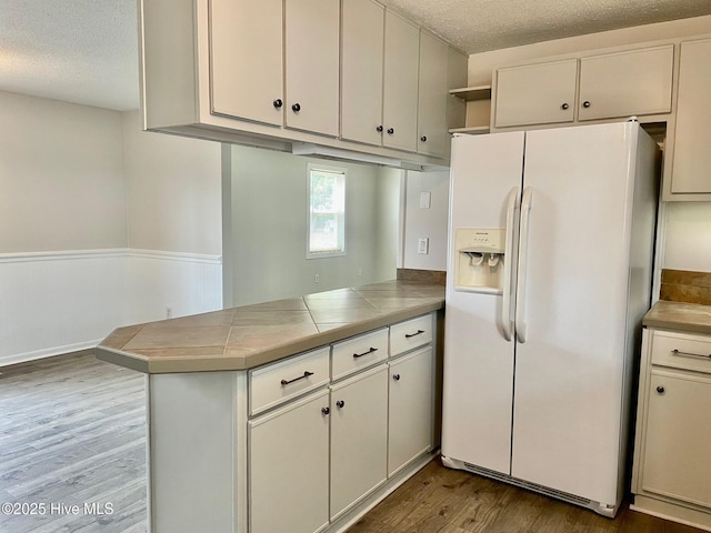 kitchen featuring hardwood / wood-style floors, tile countertops, white fridge with ice dispenser, kitchen peninsula, and a textured ceiling