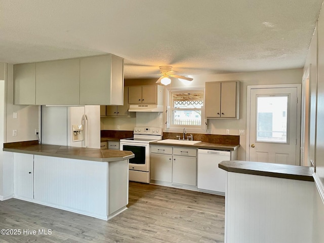 kitchen with sink, white appliances, kitchen peninsula, a textured ceiling, and light hardwood / wood-style flooring