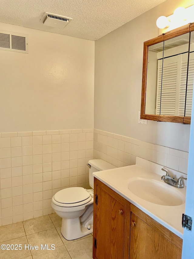 bathroom with tile patterned flooring, tile walls, vanity, a textured ceiling, and toilet