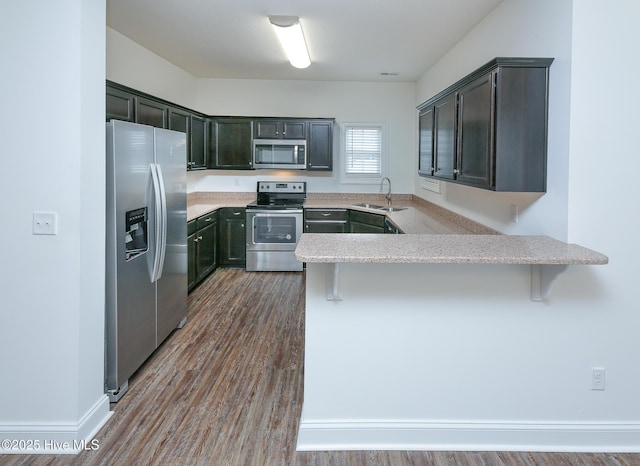 kitchen featuring appliances with stainless steel finishes, a kitchen bar, kitchen peninsula, and sink