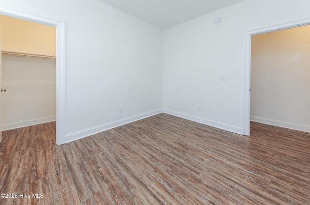 unfurnished bedroom with a closet, a walk in closet, and dark hardwood / wood-style floors