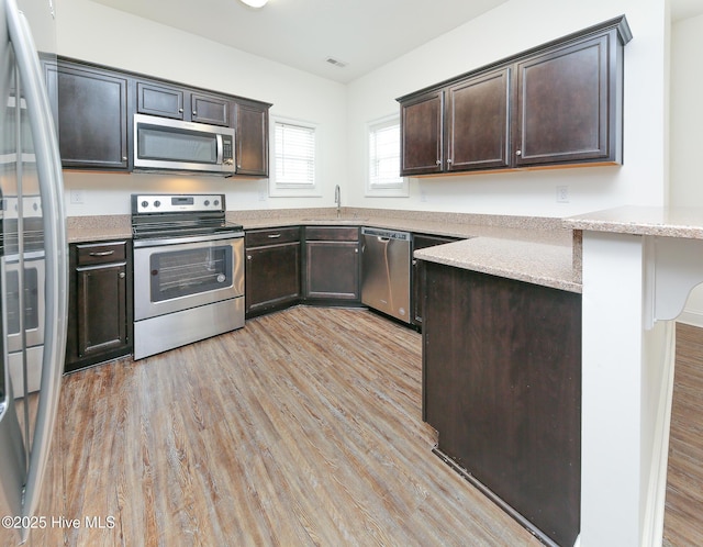 kitchen featuring dark brown cabinets, stainless steel appliances, and light hardwood / wood-style floors