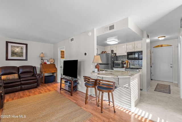 kitchen with visible vents, freestanding refrigerator, black microwave, a peninsula, and a kitchen breakfast bar