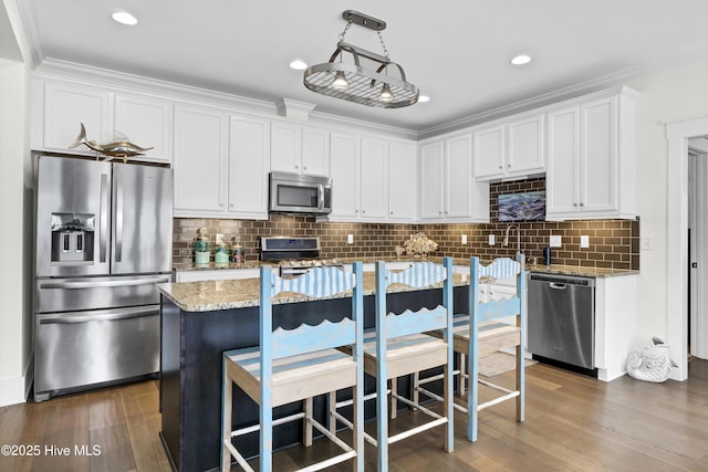 kitchen with decorative light fixtures, white cabinetry, a center island, light stone counters, and stainless steel appliances