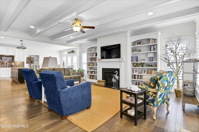 living room featuring sink, crown molding, wood-type flooring, beamed ceiling, and ceiling fan