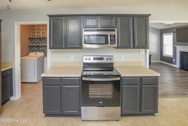 kitchen featuring stainless steel appliances, washer / clothes dryer, a textured ceiling, and light tile patterned floors