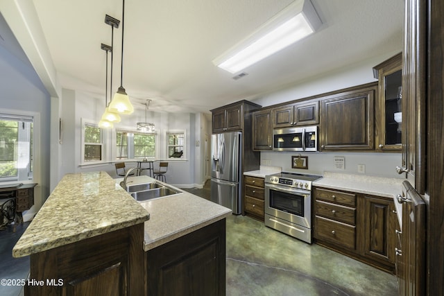 kitchen with appliances with stainless steel finishes, sink, hanging light fixtures, a kitchen island with sink, and dark brown cabinetry