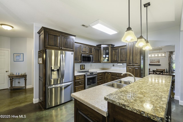 kitchen featuring pendant lighting, sink, a kitchen island with sink, stainless steel appliances, and dark brown cabinetry