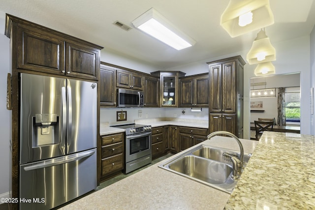 kitchen with dark brown cabinetry, sink, hanging light fixtures, and appliances with stainless steel finishes