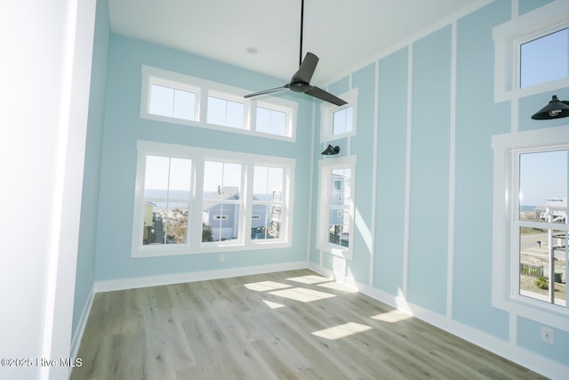 5228 E Beach Dr, Oak Island, NC 28465 - empty room featuring a towering ceiling, wood finished floors, a healthy amount of sunlight, and a ceiling fan