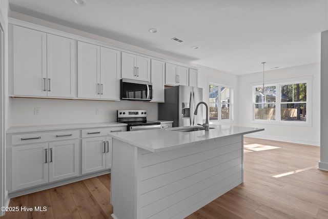 kitchen with pendant lighting, sink, white cabinetry, stainless steel appliances, and an island with sink