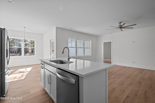 kitchen featuring sink, decorative light fixtures, light hardwood / wood-style flooring, appliances with stainless steel finishes, and a kitchen island with sink