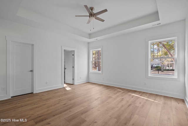 unfurnished room featuring ceiling fan, a raised ceiling, and light wood-type flooring