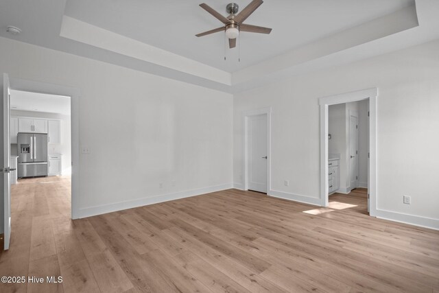 unfurnished room with ceiling fan, light wood-type flooring, and a tray ceiling