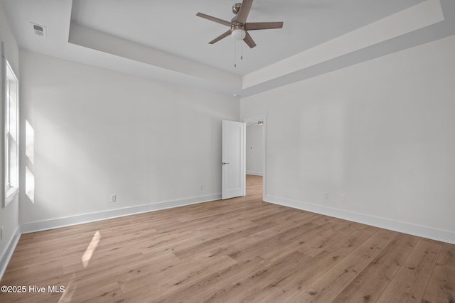 unfurnished room featuring ceiling fan, a raised ceiling, and light wood-type flooring