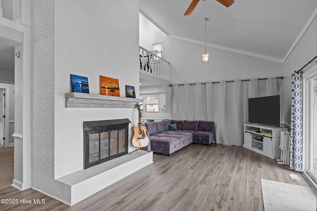 living room featuring high vaulted ceiling, a brick fireplace, and wood finished floors