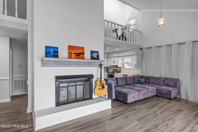 living room featuring a towering ceiling, a fireplace, visible vents, and wood finished floors