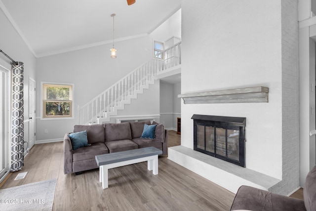 living room featuring stairway, crown molding, a glass covered fireplace, wood finished floors, and high vaulted ceiling