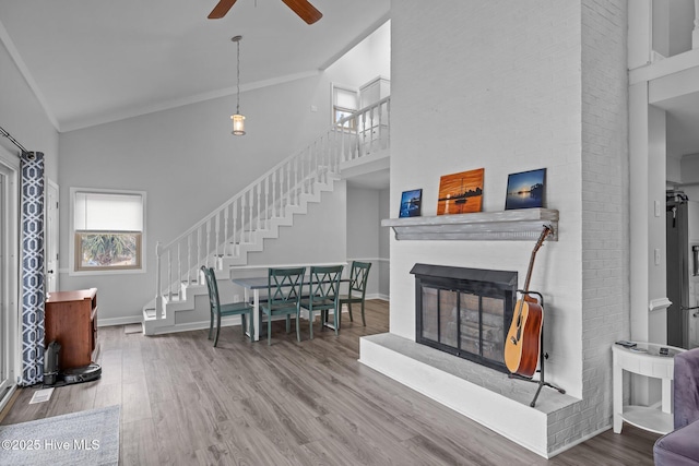 living area featuring a glass covered fireplace, wood finished floors, high vaulted ceiling, baseboards, and stairs