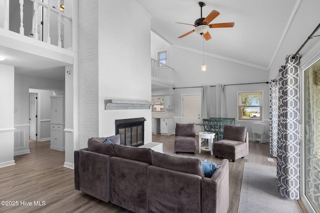 living area featuring high vaulted ceiling, a ceiling fan, wood finished floors, a glass covered fireplace, and baseboards