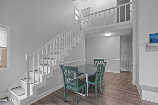 dining space featuring wood finished floors, stairway, a towering ceiling, and visible vents