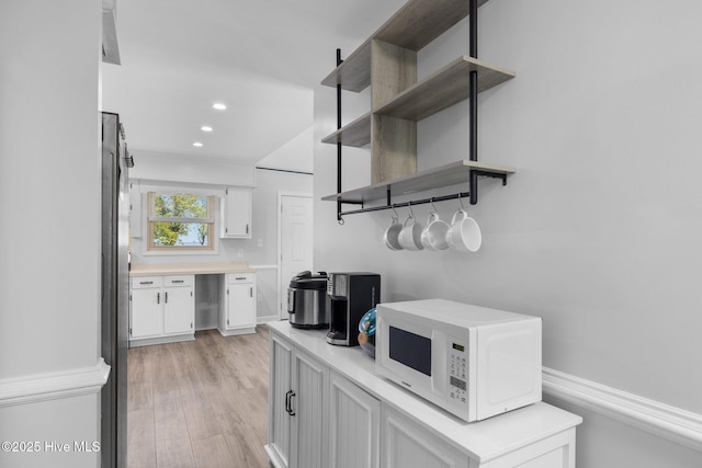 kitchen with white microwave, open shelves, light countertops, white cabinetry, and light wood-type flooring