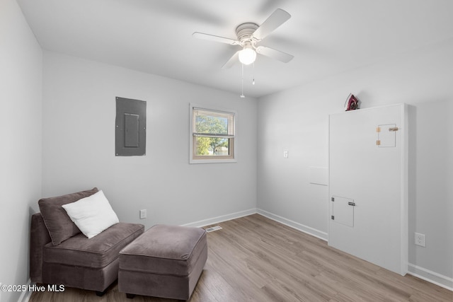 living area with electric panel, a ceiling fan, light wood finished floors, and baseboards