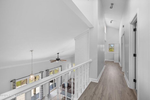 hallway with an upstairs landing, lofted ceiling, wood finished floors, and baseboards