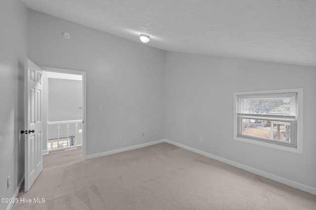 carpeted empty room with lofted ceiling, a textured ceiling, and baseboards