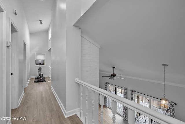 corridor with baseboards, a high ceiling, an upstairs landing, and wood finished floors