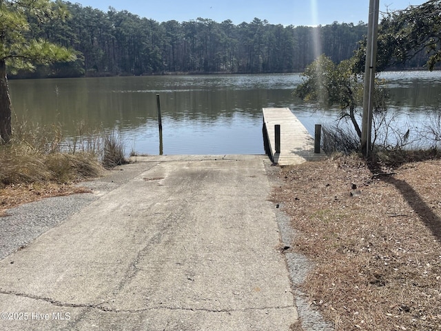 dock area with a boat ramp, a water view, and a forest view