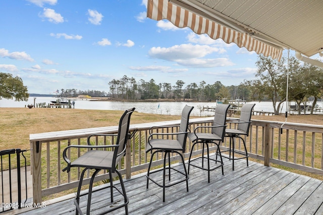 wooden terrace featuring a water view and a lawn