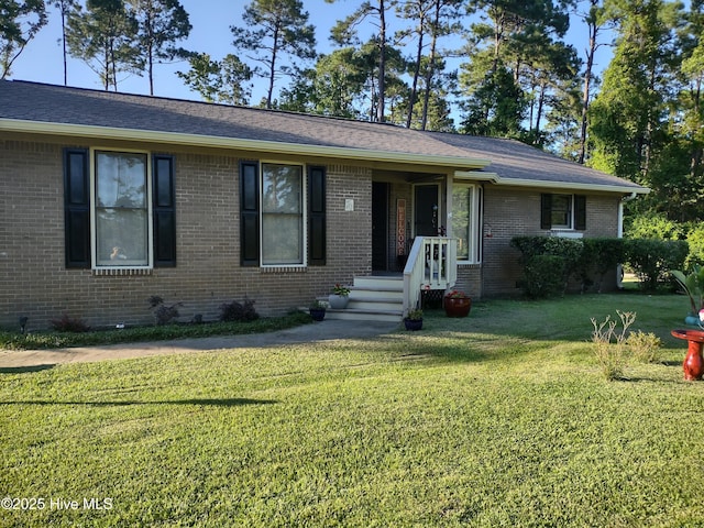 ranch-style house with a front lawn, roof with shingles, and brick siding