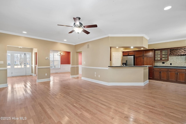 unfurnished living room featuring crown molding, ceiling fan with notable chandelier, and light hardwood / wood-style floors