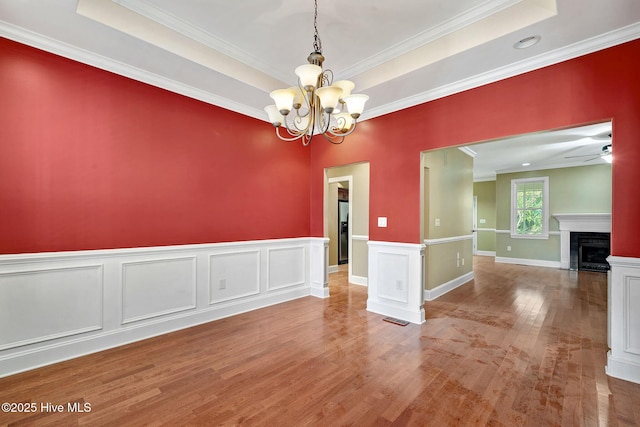 spare room with crown molding, hardwood / wood-style flooring, ceiling fan with notable chandelier, and a raised ceiling