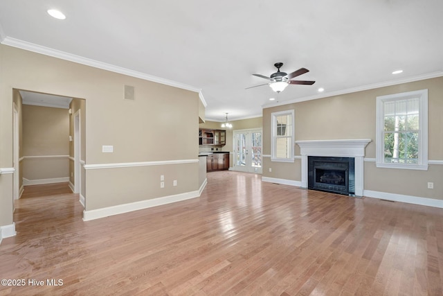 unfurnished living room with crown molding, ceiling fan with notable chandelier, and light wood-type flooring