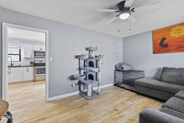 living room featuring ceiling fan, a textured ceiling, and light wood-type flooring