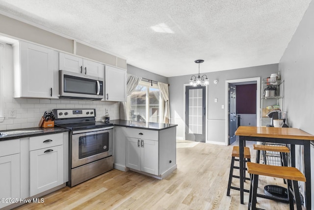 kitchen featuring white cabinetry, hanging light fixtures, light hardwood / wood-style floors, and appliances with stainless steel finishes