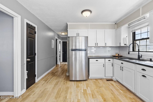 kitchen with sink, light hardwood / wood-style flooring, stainless steel refrigerator, white cabinetry, and backsplash