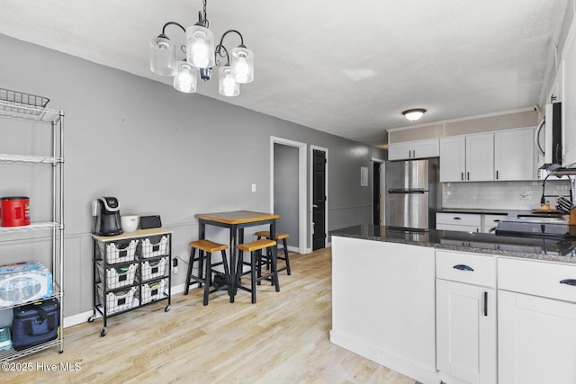 kitchen with white cabinetry, decorative light fixtures, stainless steel appliances, and dark stone counters